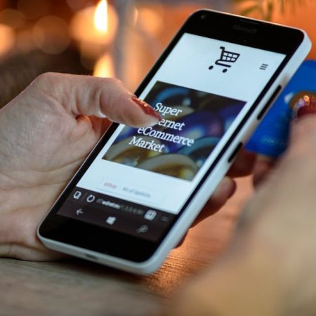 pexels-photo-230544-230544 Woman using smartphone for online shopping with credit card in hand, festive background lighting.