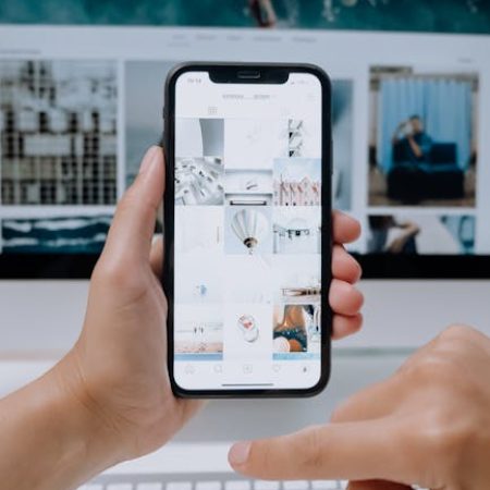pexels-photo-5082578-5082578 Person using smartphone to browse photos, office desktop setup.
